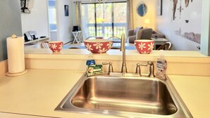 A kitchen with a stainless steel sink, red and white flowered bowls, and a bottle of hand soap.
