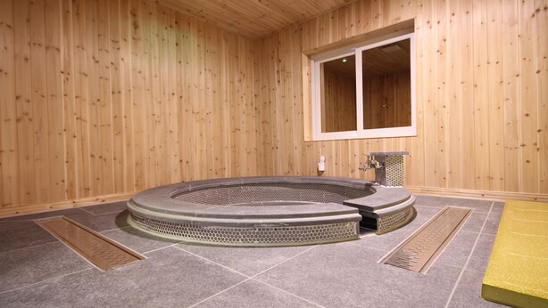 A wooden-paneled room with a stone-tiled floor, a circular hot tub, and a window. - Hotel Lesign (Busan)