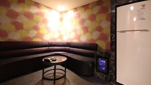A modern room with a sectional sofa, a small round table, a refrigerator, and a wall with a floral pattern. - Hotel Lesign (Busan)