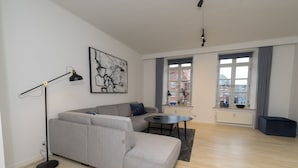 Una sala de estar moderna con un sofá seccional gris, una lámpara de pie negra, una mesa de centro negra y un ventanal con vistas a edificios.