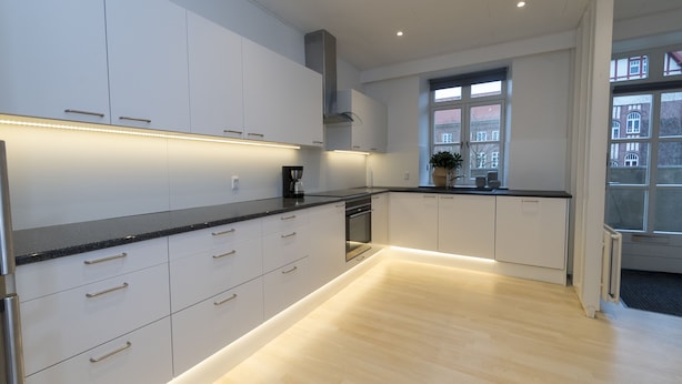 Una cocina moderna con armarios blancos, encimera negra y suelo de madera.