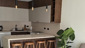 A modern kitchen with a central island, wooden stools, pendant lighting, and a large potted plant. - Dahan Sirena lighthouse luxury apartment (Paphos)