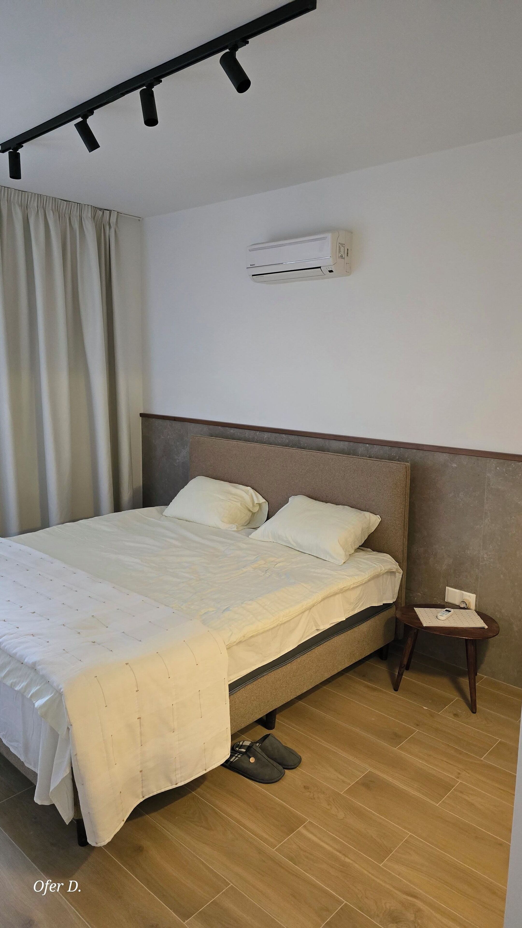 A neatly made bed with a headboard, a small bedside table with a phone, and an air conditioning unit on the wall.