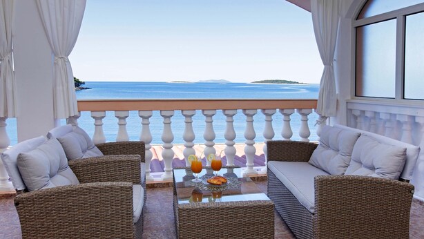 Un balcon agrémenté de meubles en osier, une table en verre avec une boisson, et une vue sur la mer.
