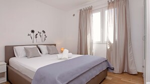 Une chambre à coucher avec un lit, des oreillers, une table de chevet, une lampe et une fenêtre avec des rideaux.