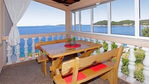 Une table et un banc en bois sont installés sur un balcon d’où l’on peut admirer la mer.