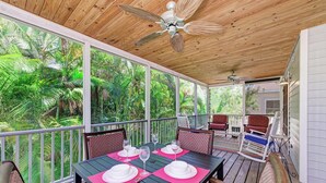 A covered outdoor dining area with a table set for four, surrounded by chairs, and a view of lush greenery.