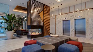 A modern lobby with a fireplace, seating area, and elevators.