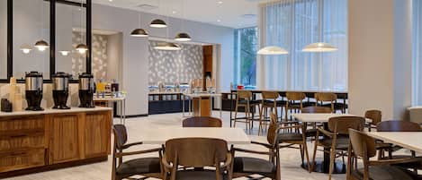 A modern restaurant with wooden furniture, pendant lighting, and a view of the outdoors through large windows.
