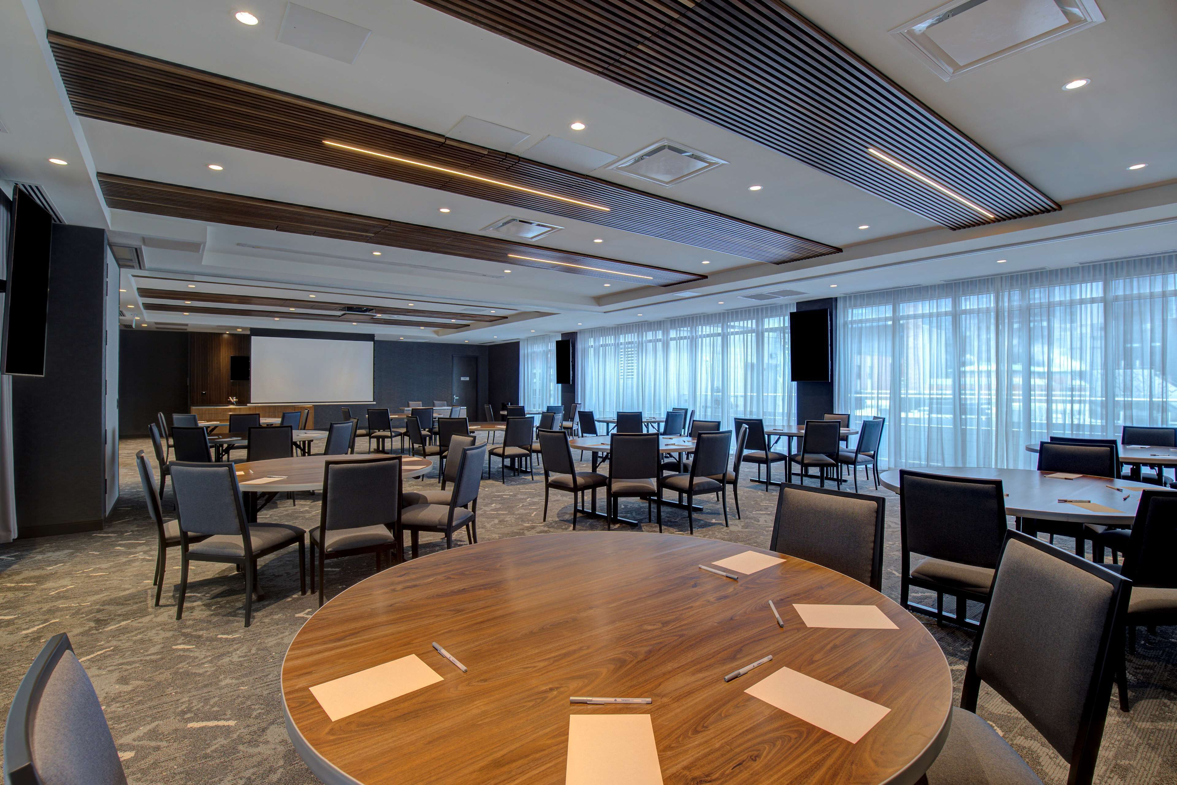 A conference room with a large wooden table, multiple chairs, and a projector screen.