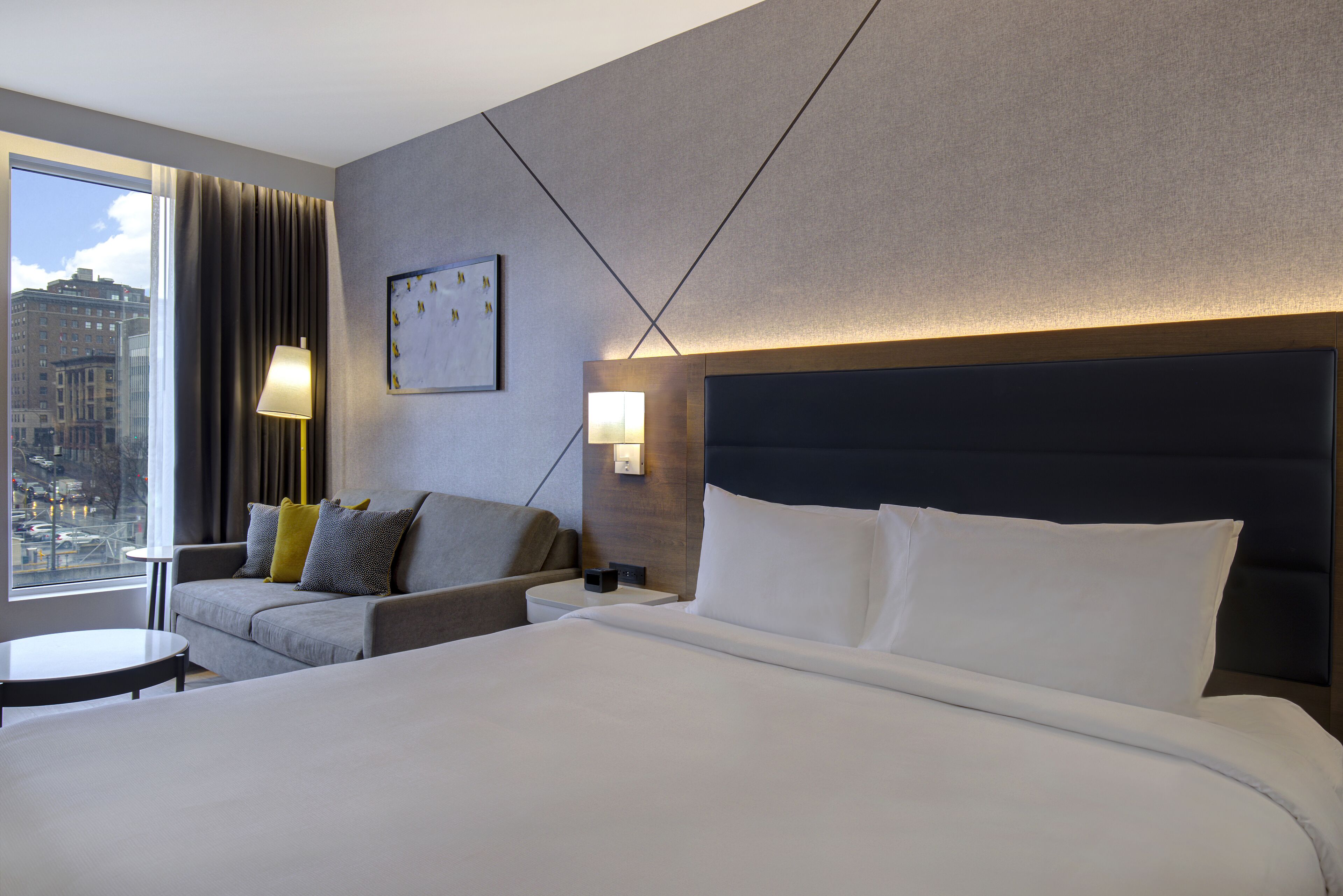 Una habitación de hotel con una cama grande, un sofá, una mesita y vistas a la ciudad.