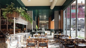 A restaurant with a bar area, wooden tables, and chairs, and large windows offering a view of the street.