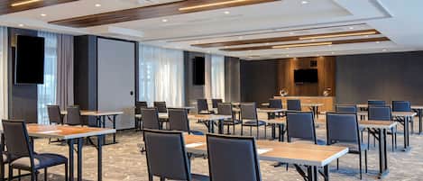 Un salón de conferencias con varias mesas y sillas, una pantalla grande y un techo con paneles de madera.