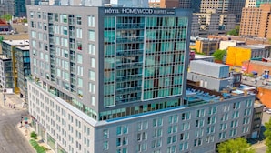 A modern hotel with a glass facade, multiple floors, and a prominent sign for 'Hotel Homewood Suites by Hilton'.