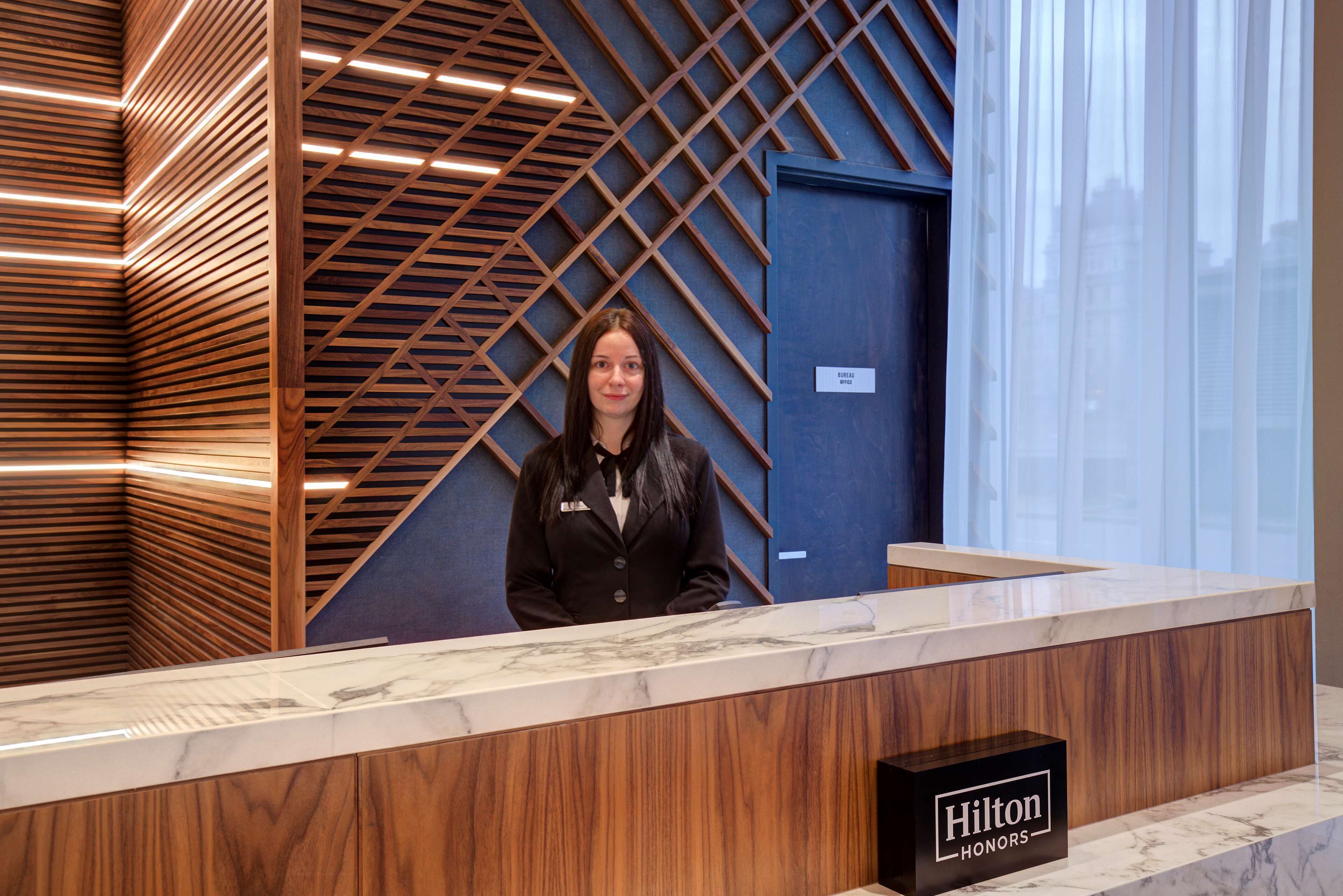 Un mostrador de recepción con diseño de panel de madera y encimera de mármol. Un cartel indica que pertenece al programa Hilton Honors.