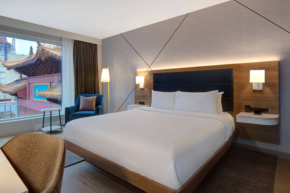 A hotel room with a large bed, two bedside tables with lamps, a chair, and a view of a traditional building.