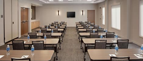 A conference room with multiple tables, chairs, and water bottles.
