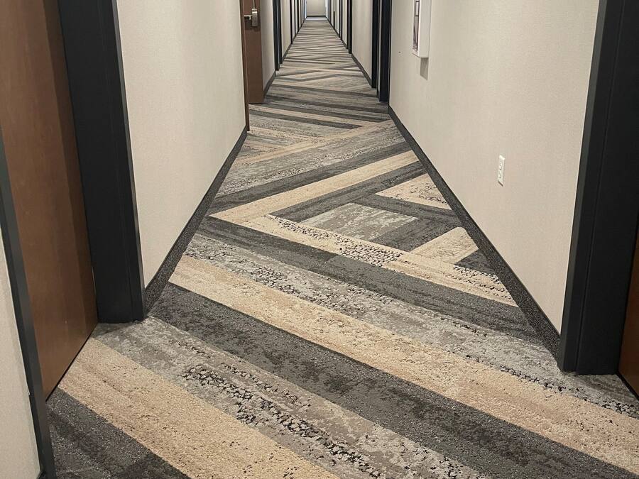 Pasillo de hotel con alfombra estampada, puertas a ambos lados y un cartel que indica la ubicación del ascensor.
