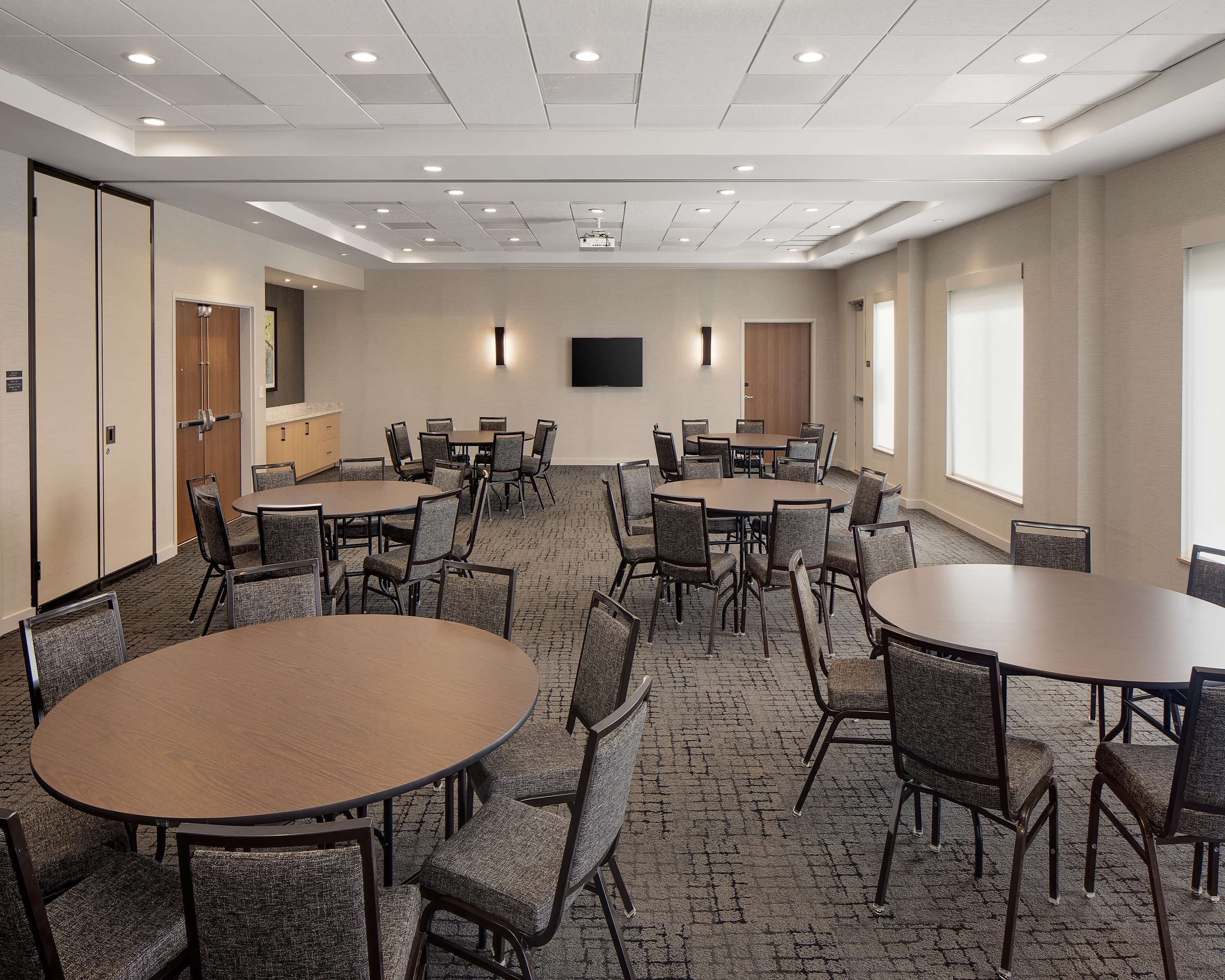 A conference room with multiple tables and chairs, a flat-screen TV, and a carpeted floor.