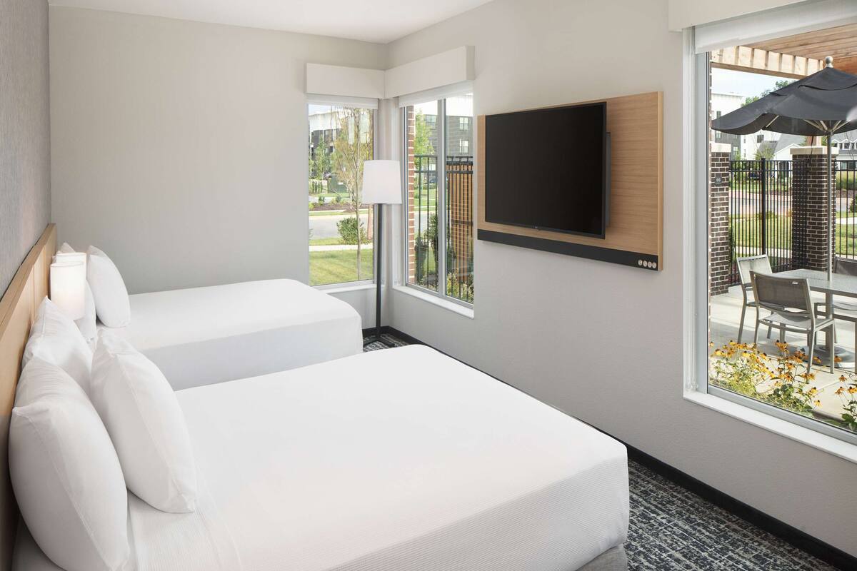 Quarto de hotel com duas camas, televisão presa na parede e vista para o pátio externo.