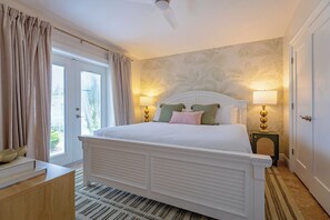 Ein Schlafzimmer mit einem Bett, zwei Nachttischlampen, einer Tür und einem Fenster mit Vorhängen.