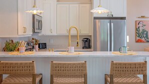 Een keuken met witte kastjes, een roestvrijstalen koelkast en een centraal eiland met stoelen.