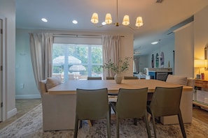 Uma sala de jantar com uma mesa grande, quatro cadeiras, um candelabro e vista para o exterior através de grandes janelas.