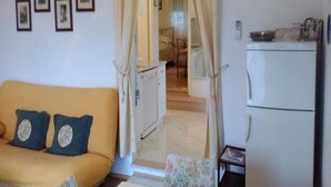 A living room with a sofa, a small table, and a kitchen area with a refrigerator. - Apartment Agata (Supetar)