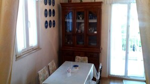 A dining area with a table, chairs, a cabinet with glass doors, and a window with curtains. - Apartment Agata (Supetar)