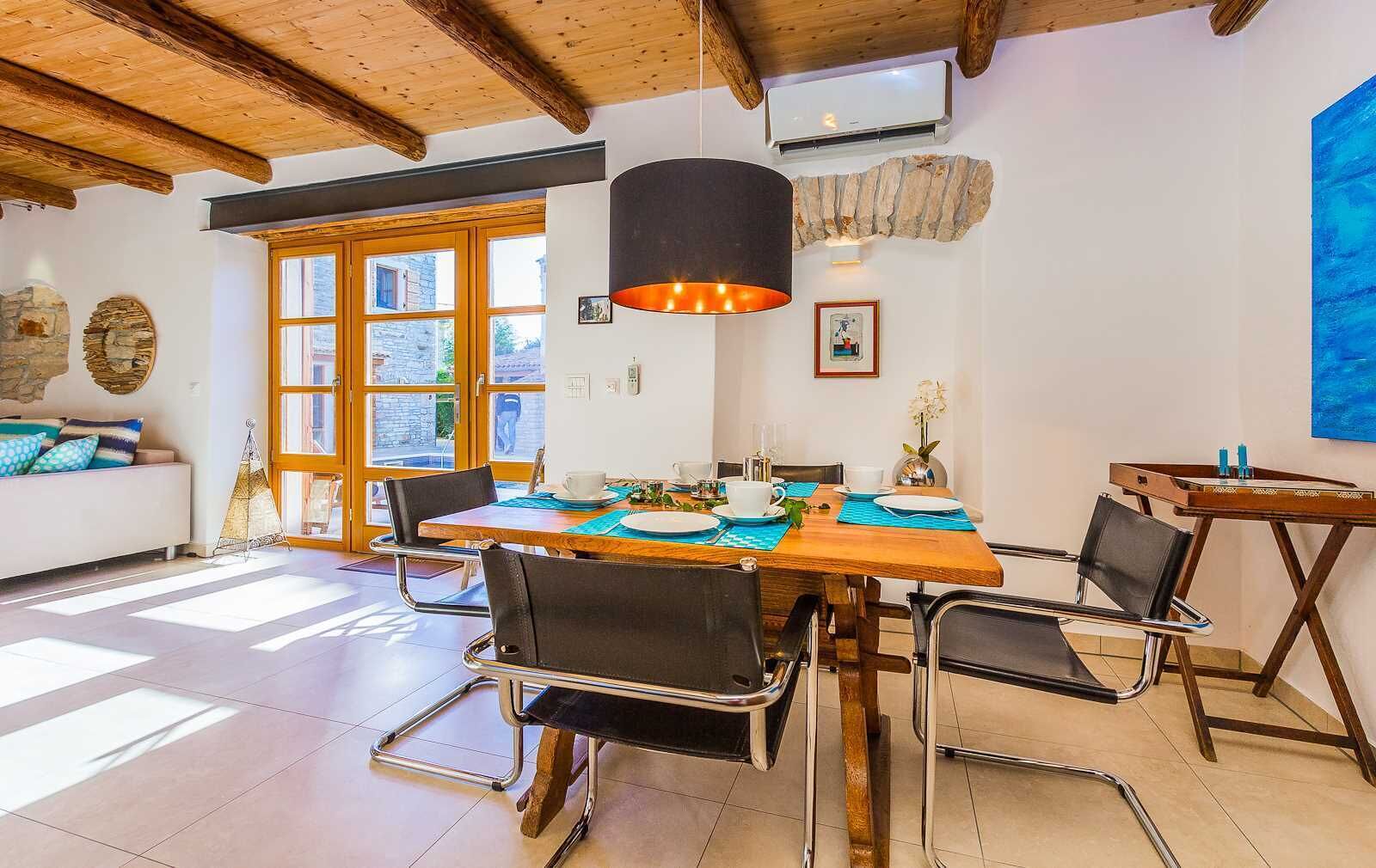 Un espace repas avec une table en bois, des chaises noires et un luminaire suspendu.