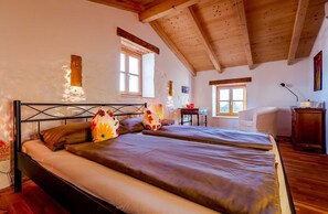 A bedroom with two beds, wooden beams, a desk, and a chair.