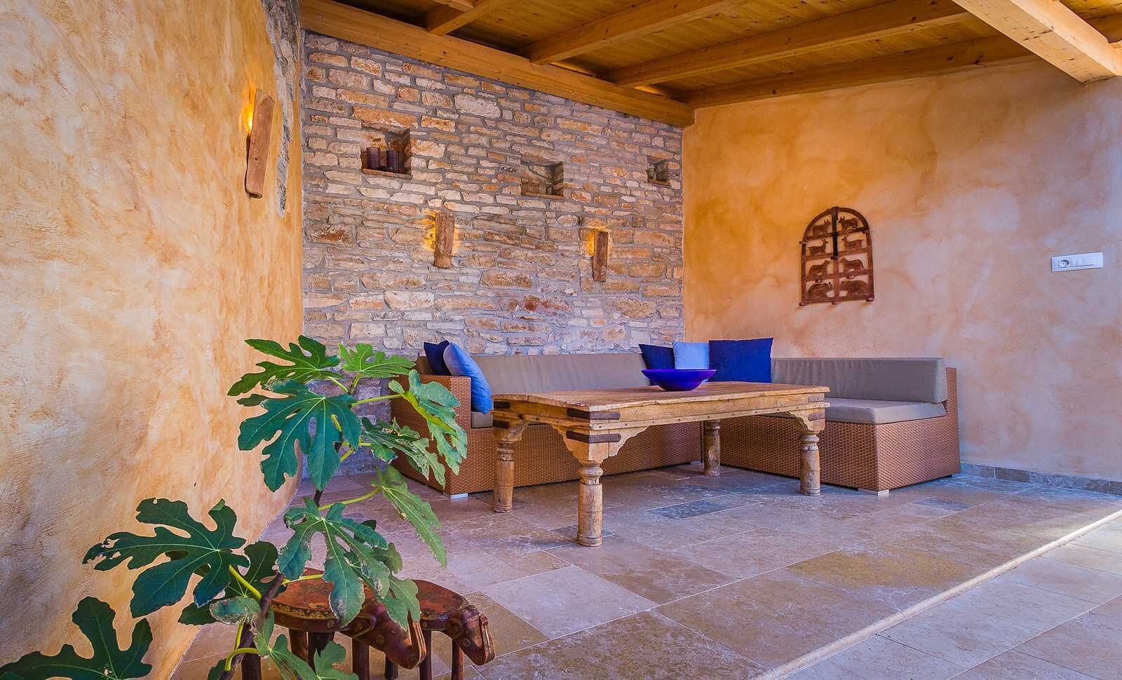 A rustic stone wall, a wooden table, wicker furniture, and a large plant.