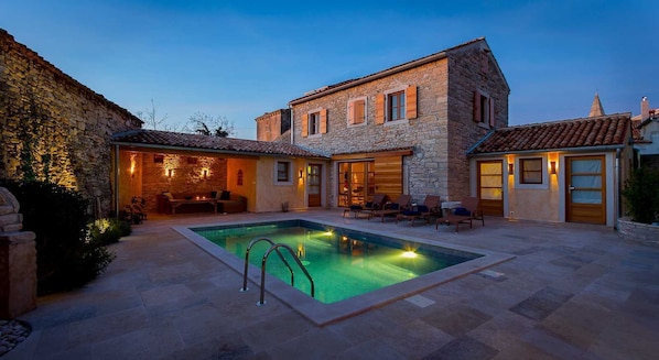 A stone building with a swimming pool, outdoor seating, and a well-lit patio area.