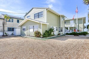 A two-story building with a front porch, a flagpole with an American flag, and a gravel driveway. - Quaint & Cozy w/Balcony ~ Port Holiday #6 (Indian Rocks Beach)