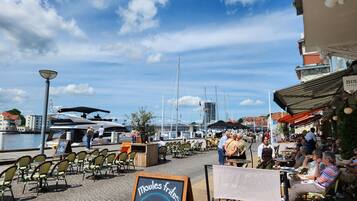 Ein Café am Wasser mit Außenbestuhlung, einem Schild für Moules-Frites und Blick auf Boote und Gebäude im Hintergrund.
