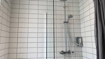 A shower with a handheld showerhead and a wall-mounted faucet, tiled walls, and a curtain.