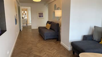 En moderne stue med fiskebensparketgulv, en mørkegrå sofa, et lille rundt bord og en gulvlampe.