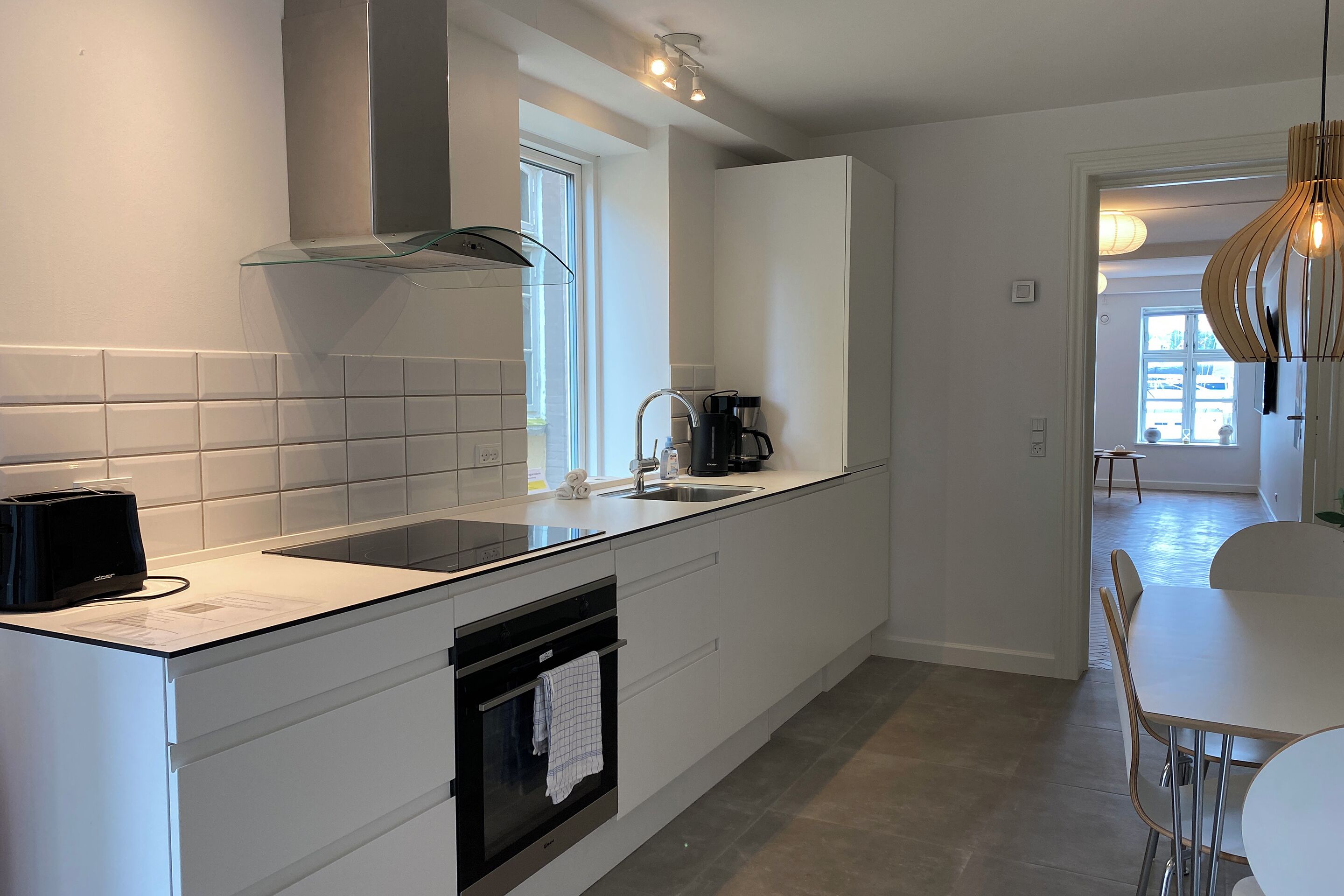 A modern kitchen with white cabinetry, a built-in oven, a coffee maker, and a window providing natural light.