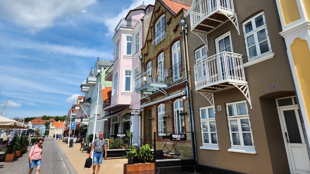 Une rue bordée de bâtiments aux couleurs vives, un café et un ciel d’un bleu éclatant.