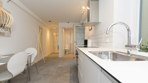 Une cuisine moderne avec des meubles blancs, un évier en acier inoxydable et un coin repas avec des chaises blanches.