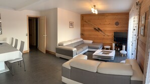 Ein modernes Wohnzimmer mit einer Eckcouch, einem Esstisch mit Stühlen, einem Fernseher und einer Wandpaneele aus Holz.