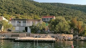 Un bâtiment situé sur la côte, avec un toit rouge, une jetée en pierre et, en arrière-plan, des collines verdoyantes.