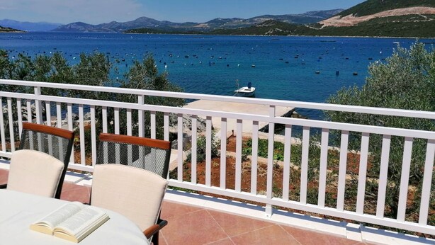 Une terrasse avec des sièges extérieurs donnant sur une zone côtière, avec des bateaux et des montagnes en arrière-plan.