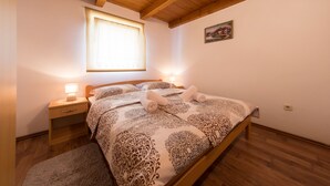 A cozy bedroom with a wooden ceiling, a large bed with patterned bedding, two bedside lamps, and a window with blinds. - Holiday home Veki (Korenica)