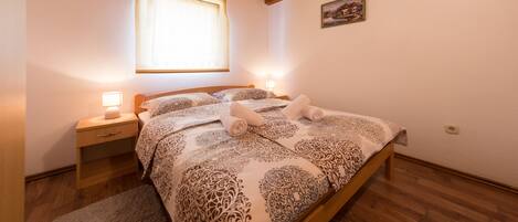 Een knus slaapkamer met een houten plafond, een groot bed met beddengoed met een patroon, twee nachtlampjes en een raam met zonwering.