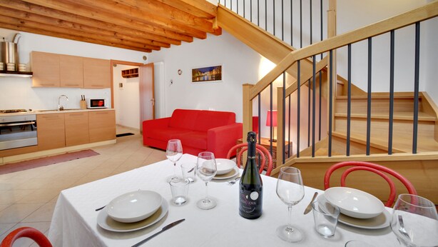Un coin repas avec une table mise pour le dîner, une bouteille de champagne et une chaise rouge.