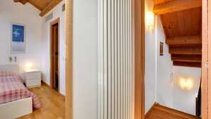 Une chambre à coucher avec un lit, une table de chevet et une commode. Le plafond est en bois et une porte donne accès à une autre pièce.