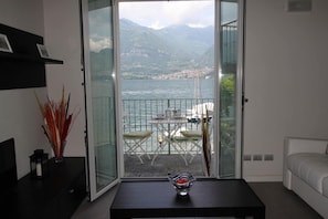 A room with a balcony overlooking a lake and mountains.