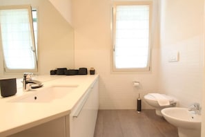 A modern bathroom with a white sink, a mirror, a toilet, and a bidet.