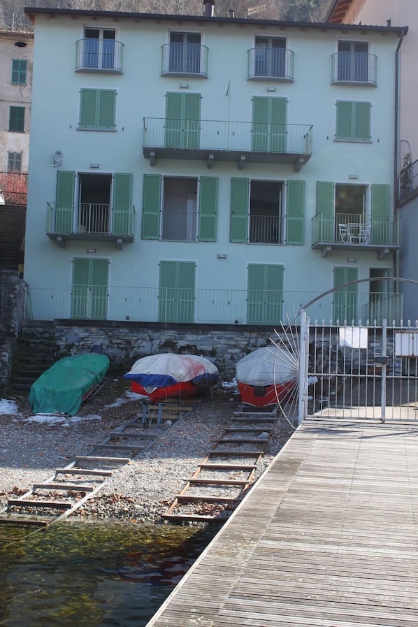 A building with multiple balconies and green shutters. There are boats covered with tarps on the ground.